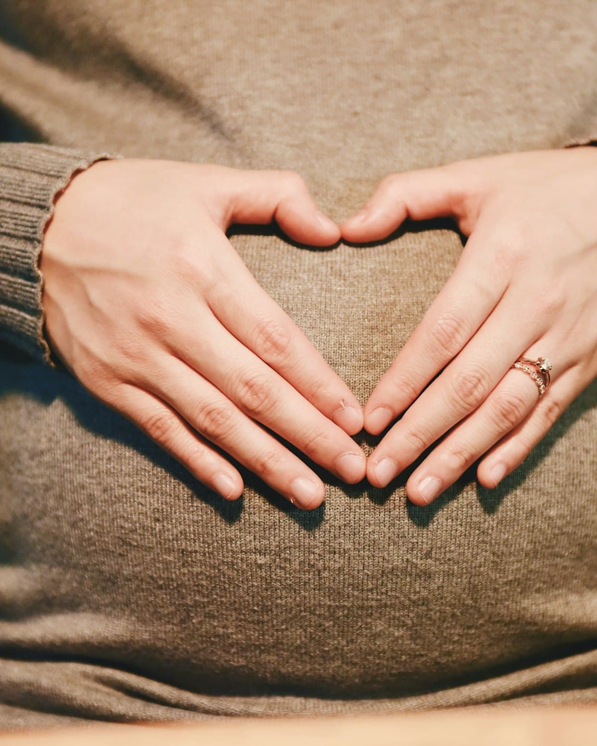 Mãos formando um coração sobre a barriga de uma gestante