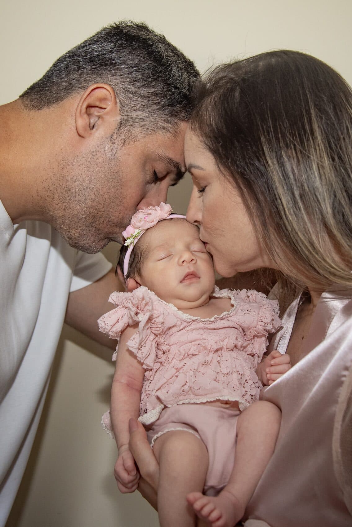 Pais beijando a filha recém-nascida que dorme no colo