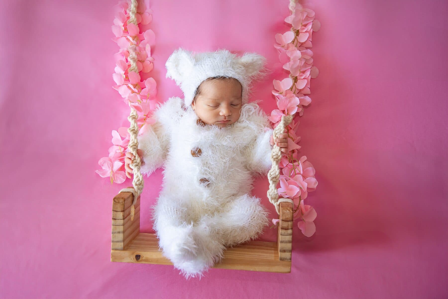 Bebê recém-nascida de touquinha dormindo em um balanço decorado com flores